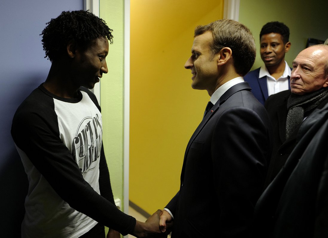 Francijas prezidents Emanuels Makrons sarokojas ar sudāniešu migrantu Kalē bēgļu centrā Ahmedu Adamu