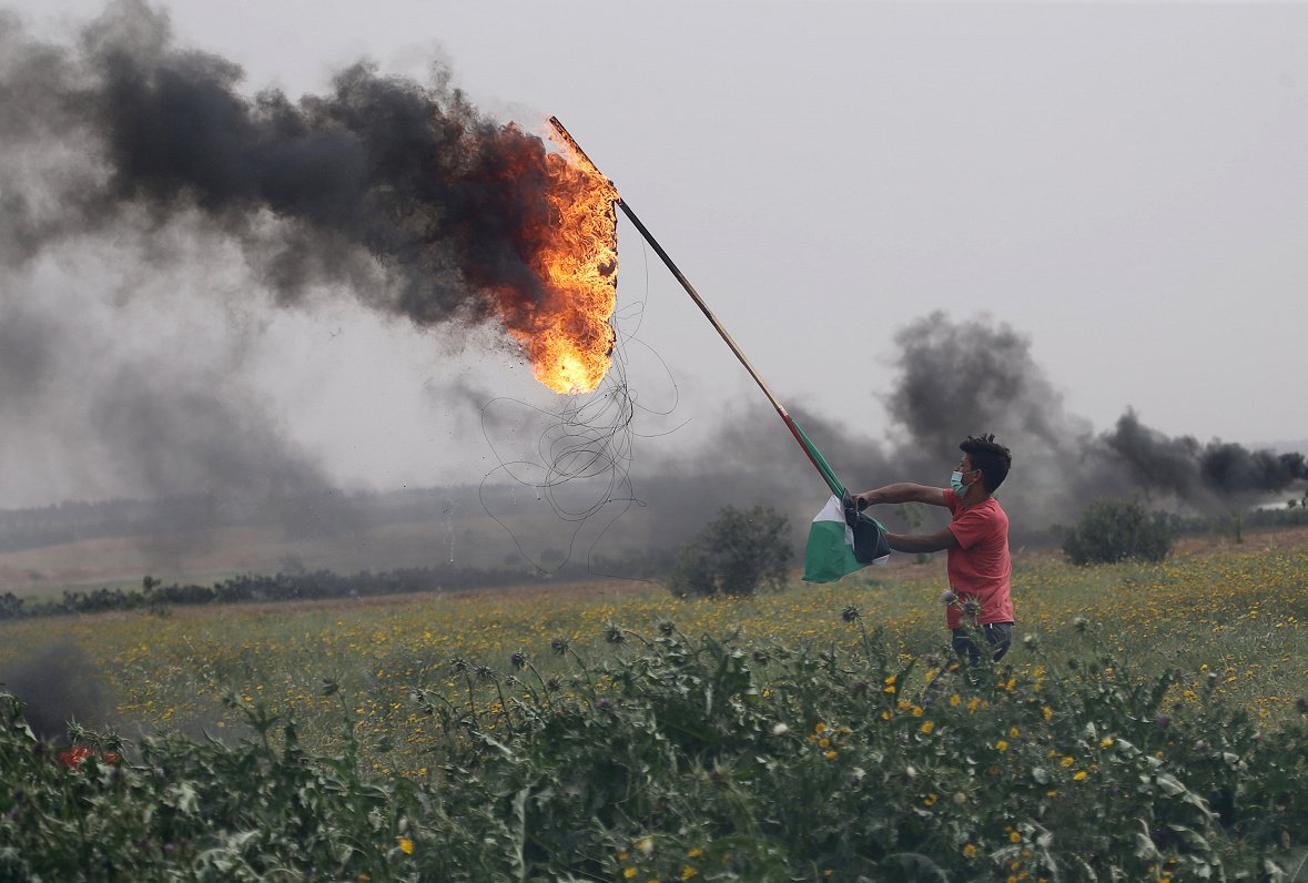Palestīniešu protestētājs tur degošu riepu 23. marta demonstrācijās