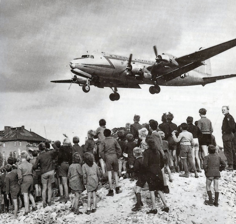 Berlīnes iedzīvotāji noraugās uz ASV transporta lidmašīnu, kas apgādā Berlīni blokādes laikā.