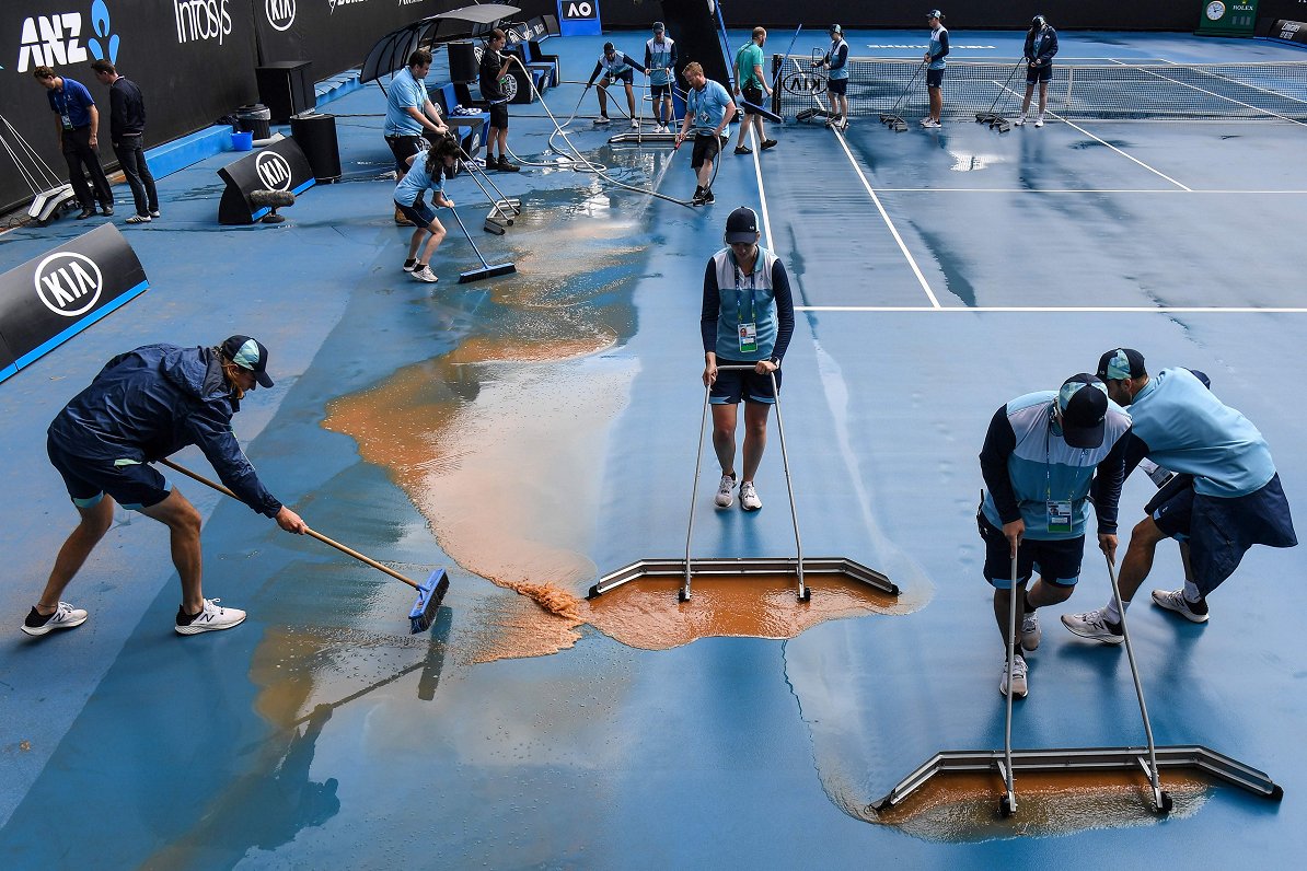Melburnā tenisa laukumu sakopj pēc dubļaina lietus