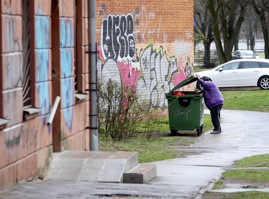 Cilvēks pie atkritumu konteinera pilsētā