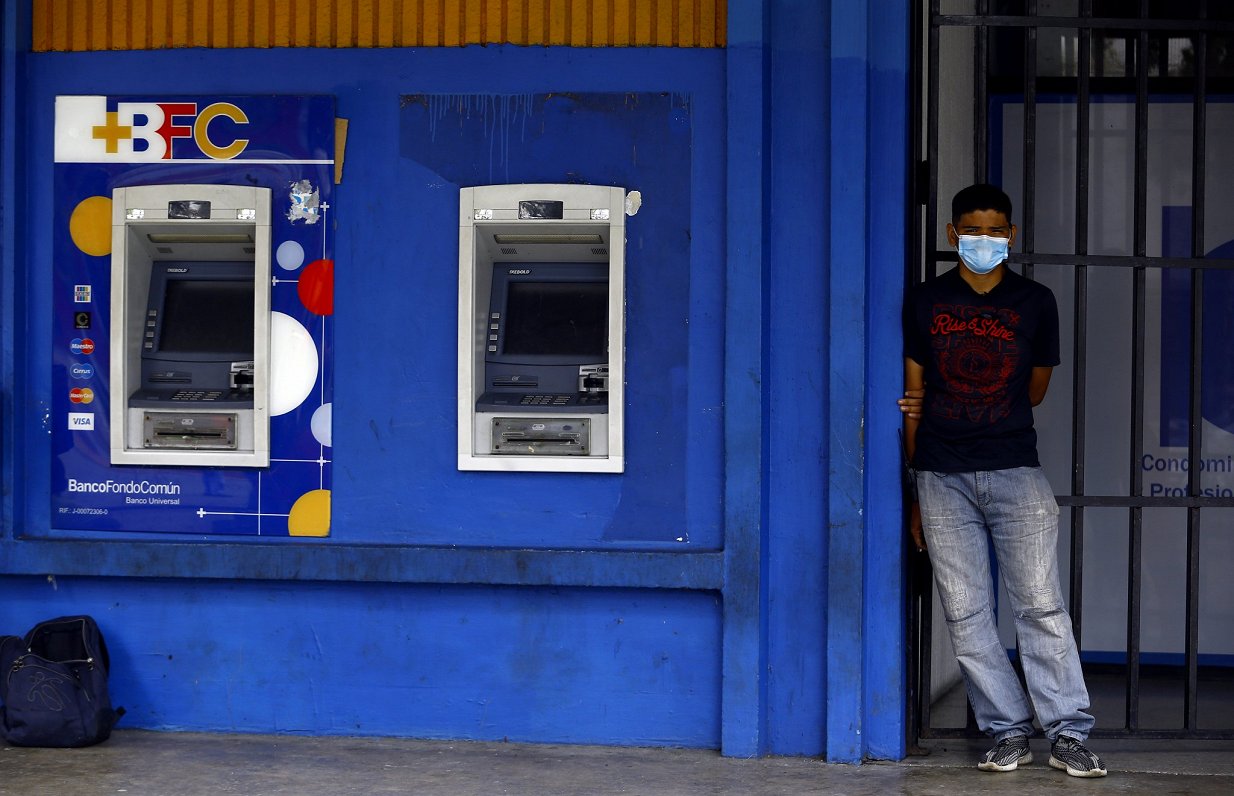 Cilvēks Covid-19 sejas maskā pie naudas izmaksas aparāta Venecuēlas pilsētā Valensijā, Karabobo reģi...