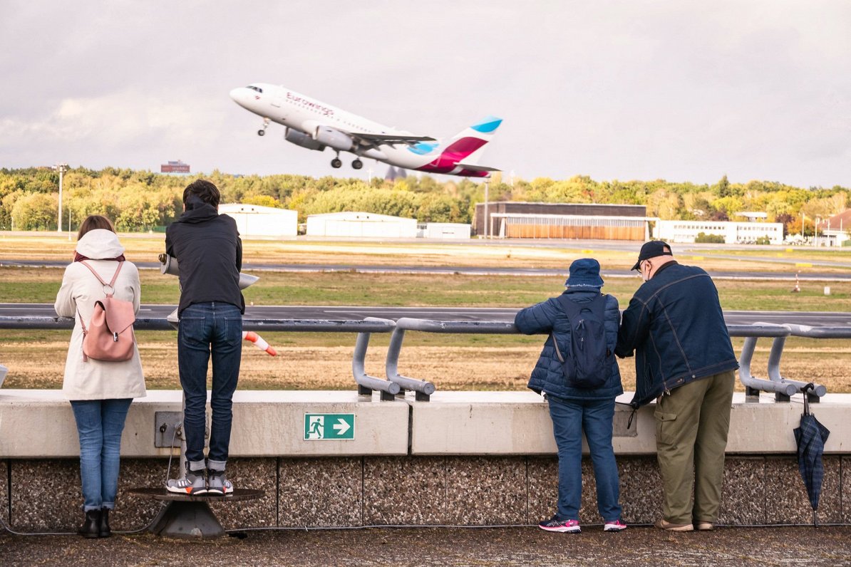 Cilvēki vēro lidmašīnas pacelšanos Berlīnes Tēgeles Oto Lilientāla lidostā. 2020. gada rudens.
