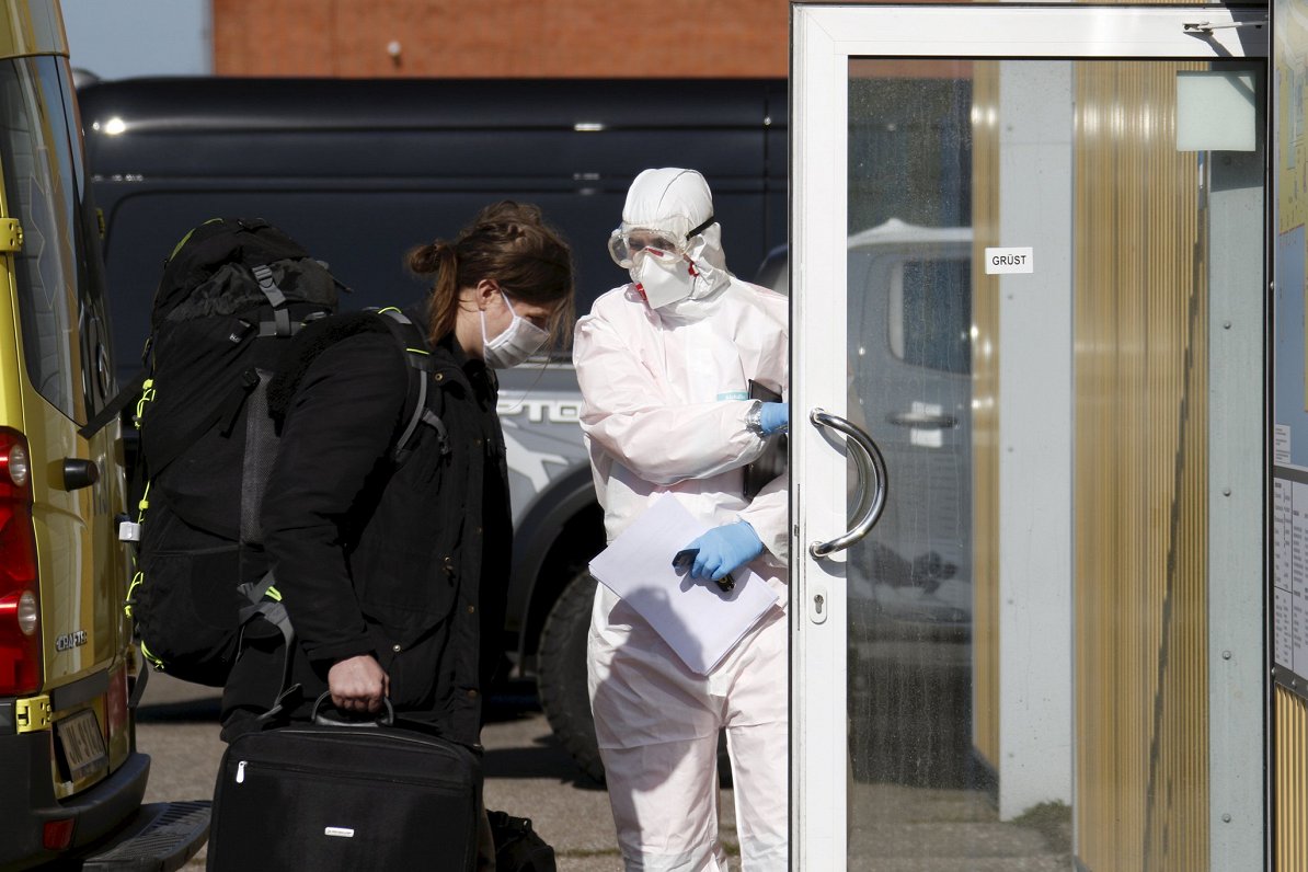 Medicīniskais personāls Covid-19 aizsargtērpā un cilvēks sejas maskā