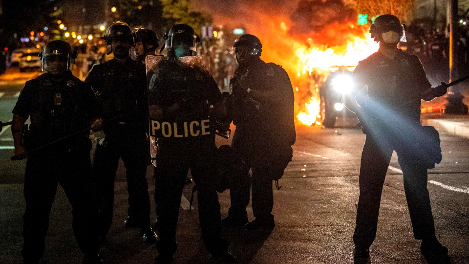 30 мая 2020 года, Вашингтон. Полицейский спецназ на фоне горящего автомобиля в одном квартале от Бел...