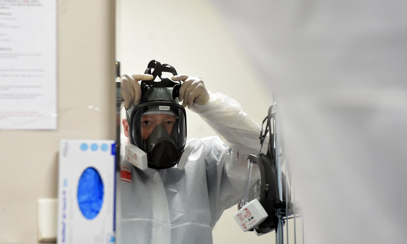 Mediķis uzvelk respiratora masku, dodoties ārstēt Covid-19 pacientus