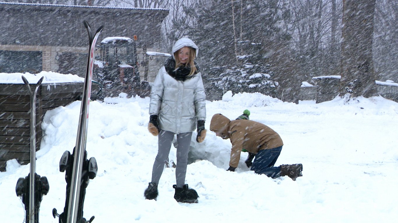 Mamma Dana vēro, kā tētis Ludvigs vada sniega būdas celtniecību