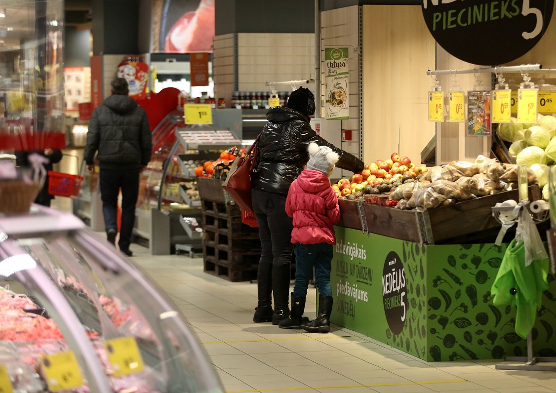Sieviete ar bērnu iepērkas lielveikala augļu un dārzeņu nodaļā.