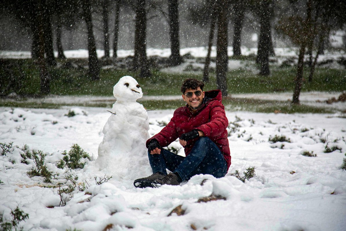Vīrietis pozē pie sniegavīra Lībijā (16.02.2021)