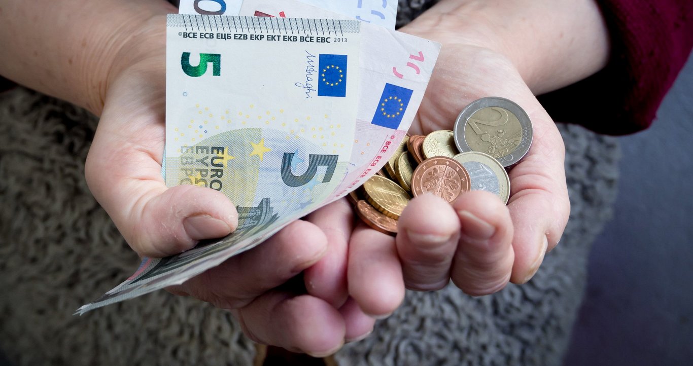 Cilvēks ar sastrādātām rokām tur rokās eiro monētas. Attēls ilustratīvs