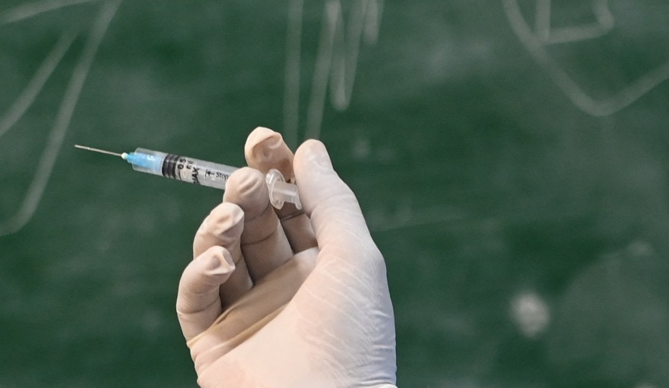 Injekcijai sagatavota Covid-19 vakcīna uz zaļas skolas tāfeles fona