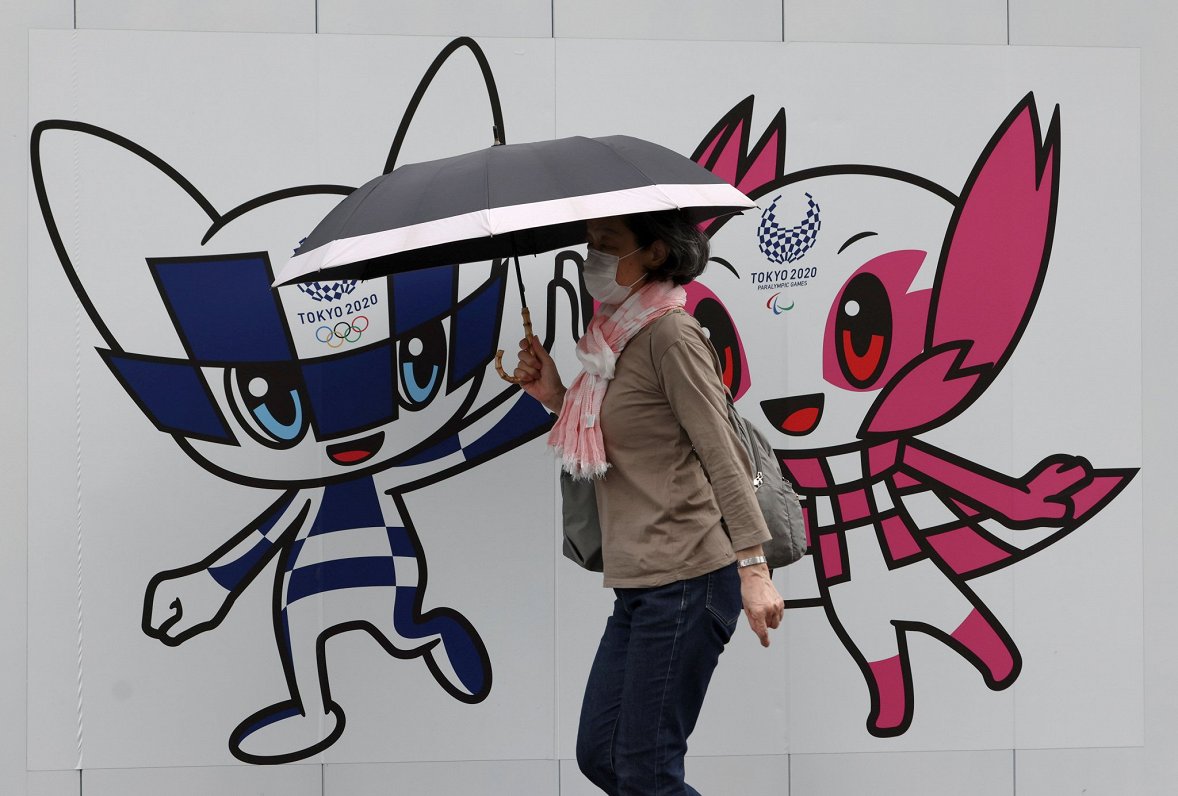 Sieviete Japānā dodas garām sienai, uz kuras attēloti Tokijas spēļu talismani