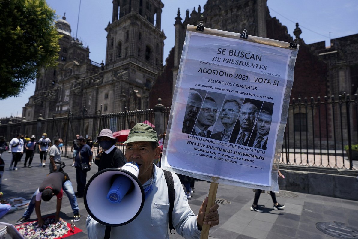 Meksikā iedzīvotājs ar plakātu, kurā redzami vairāki bijušie valsts prezidenti.