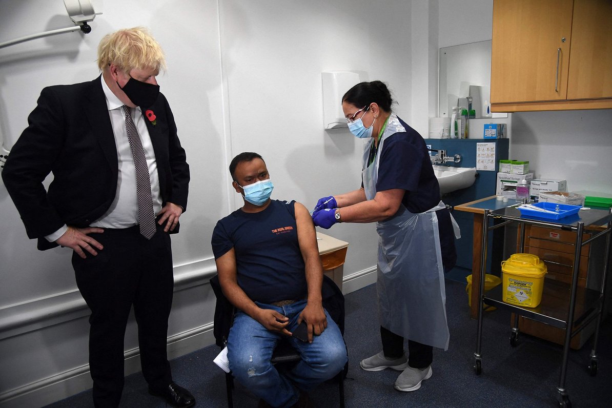 Lielbritānijas premjers Boriss Džonsons vēro, kā iedzīvotājs saņem Covid-19 vakcīnas balstdevu