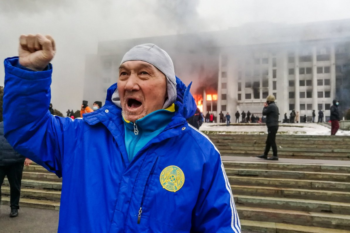 Protestētājs uz aizdedzinātās Almati pašvaldības ēkas fona