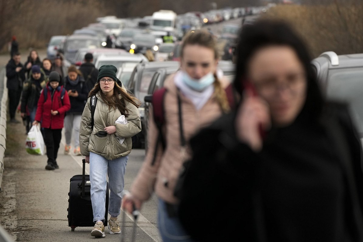 Ukrainian refugees walk along vehicles lining-up to cross the border from Ukraine into Moldova, at M...