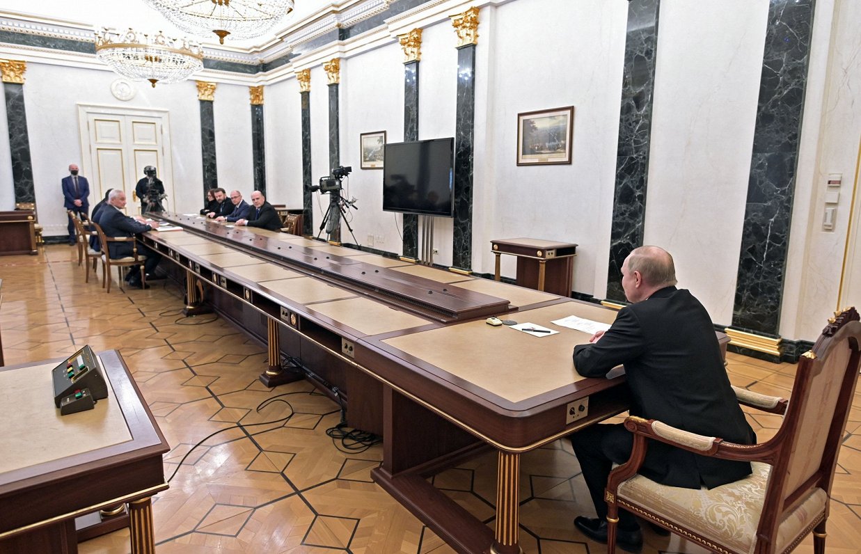 Krievijas prezidents Vladimirs Putins sarunājas ar amatpersonām, sēžot pie vairākus metrus gara gald...