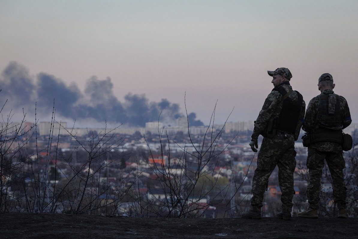 Ukrainas karavīri vēro dūmus, kas paceļas no Krievijas uzbrukumā cietušās maizes fabrikas Harkivā