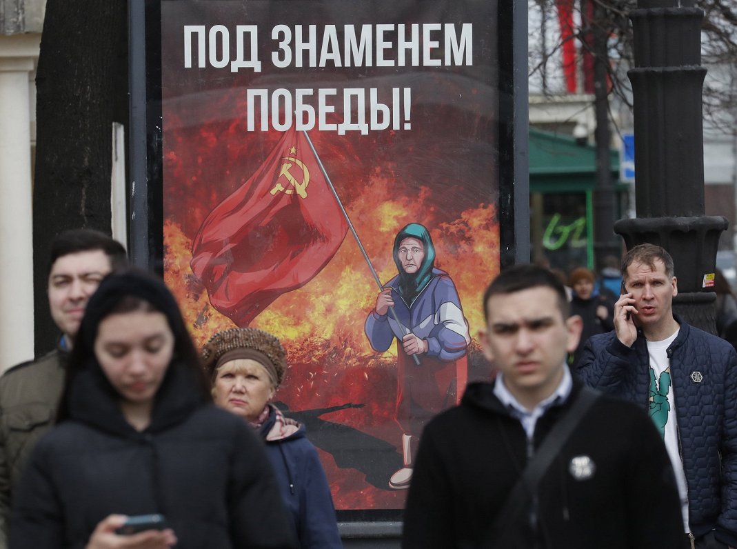 Krievijas pilsētu ielās parādījušies propagandas plakāti, kurās attēlota sirmgalve ar PSRS karogu ro...