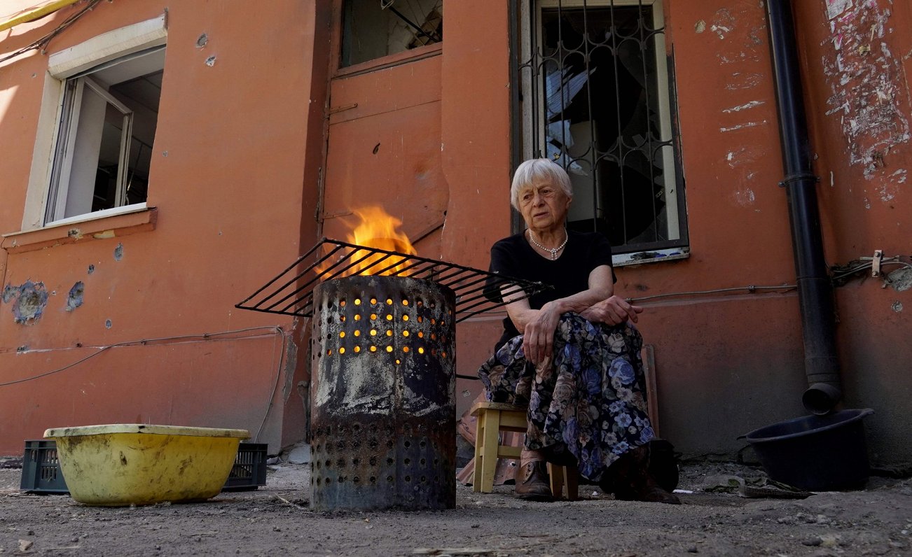 Krievijas spēku okupētajā Mariupoles pilsētā sieviete gatavo ēdienu ārpus uzbrukumā cietušās mājas
