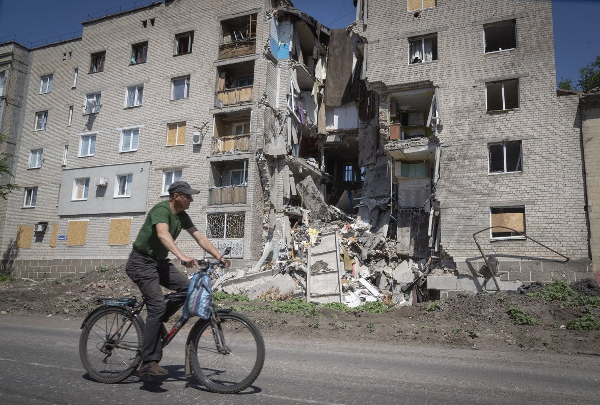 Vīrietis ar velosipēdu pie karadarbībā izpostītas ēkas Doneckas apgabalā