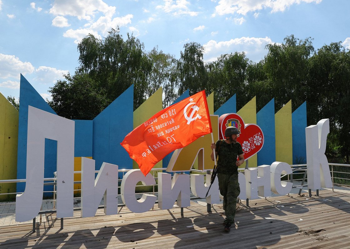 Okupantu karavīrs ar sarkano karogu pie ieņemtās Ukrainas pilsētas Lisičanskas