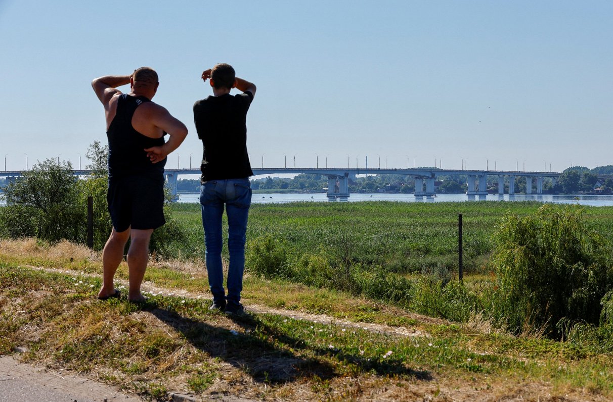 Krievijas spēku okupētajā Ukrainas pilsētā Hersonā vīrieši skatās uz tiltu, kas pēc Ukrainas bruņoto...