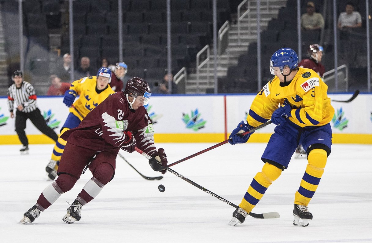 Latvijas U-20 izlases hokejists Fēlikss Gavars (pa kreisi) pasaules čempionāta spēlē pret Zviedriju