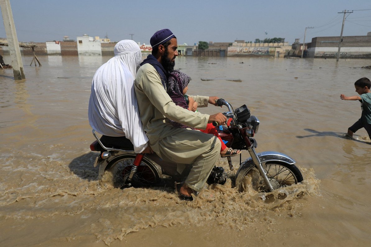 Pakistānā ģimene ar motociklu pārvietojas pa plūdu skarto apvidu