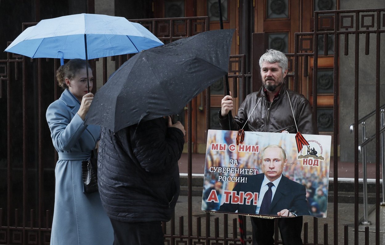 Krievijas prezidenta Vladimira Putina atbalstītājs pie Valsts domes ēkas ar plakātu &quot;Mēs ar viņ...