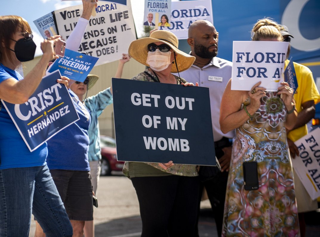 Priekšvēlēšanu mītiņš Floridas štatā. Sievietes plakāts aicina &quot;likt mierā viņas dzemdi&quot;....