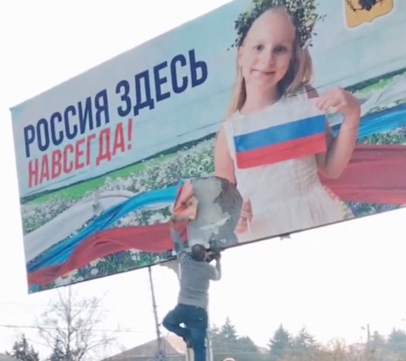 Hersonas apgabalā vīrietis plēš nost Krievijas propagandas plakātu ar uzrakstu &quot;Krievija šeit i...
