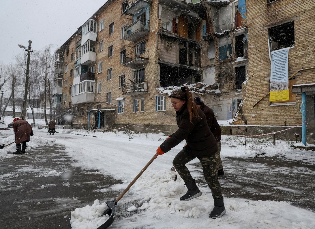 Жительница села Горенка чистит снег у дома, в котором после обстрела РФ отсутствует электричество, о...