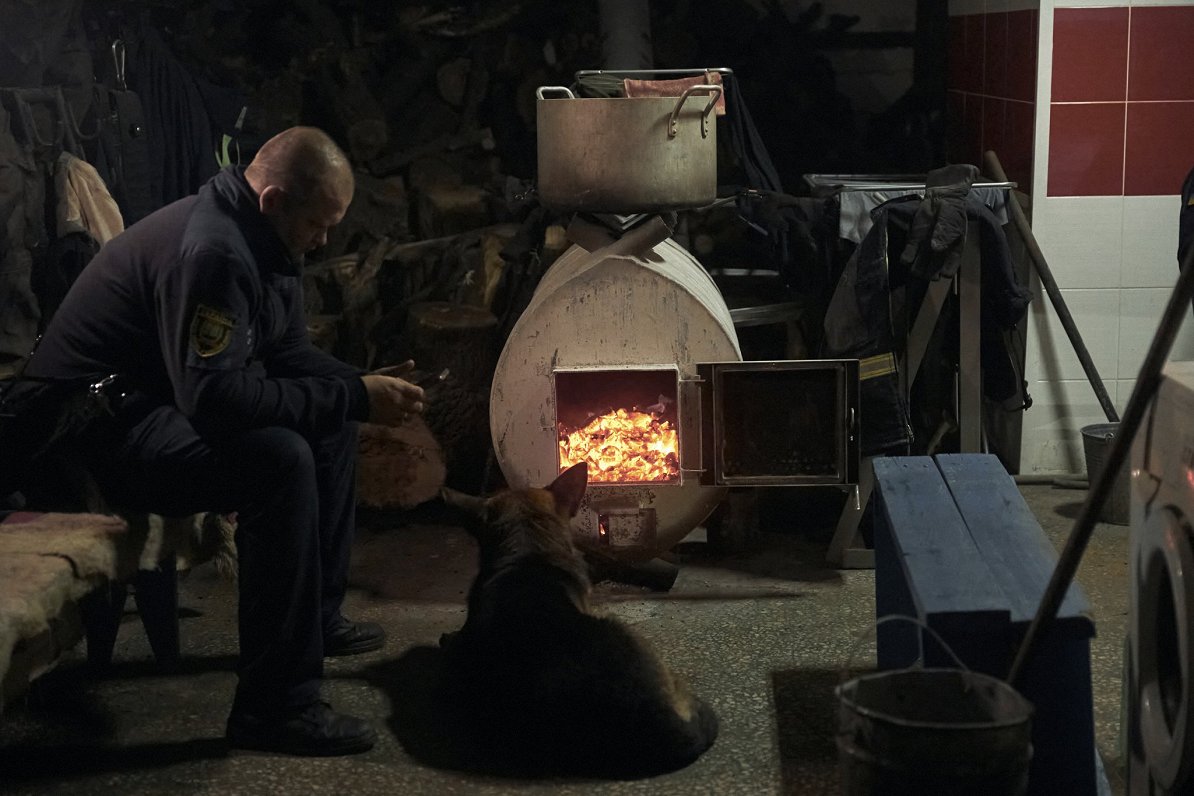 Glābšanas dienesta darbinieks ar suni sildās pie krāsns Bahmutā
