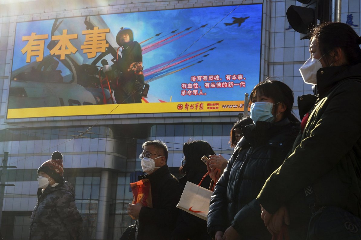 Pekinas iedzīvotāji pie plakāta, kas reklamē Ķīnas armiju