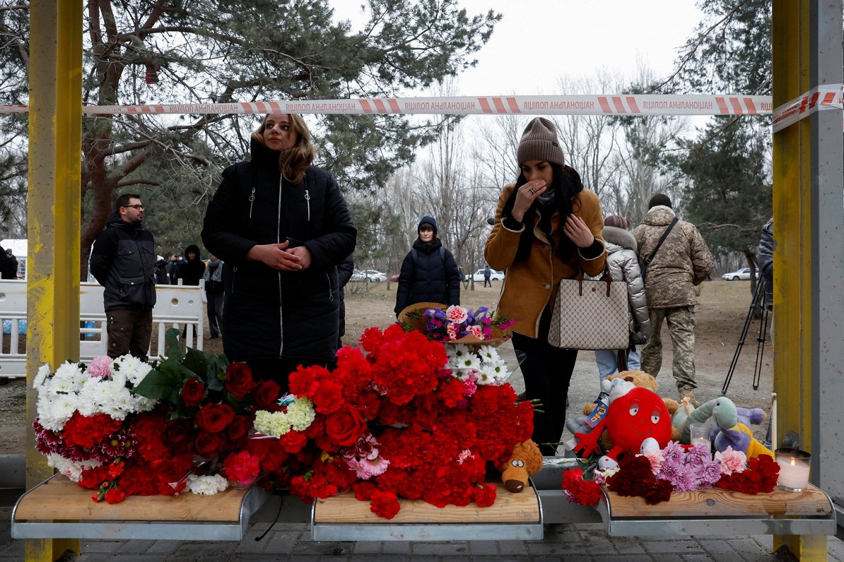 Ukrainas pilsētā Dnipro cilvēki noliek ziedus un rotaļlietas Krievijas raķetes triecienā nogalināto...