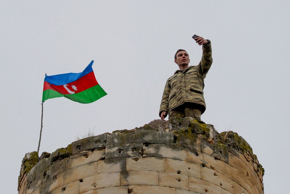 Azerbaidžānas karavīrs fotografējas ar valsts karogu fonā