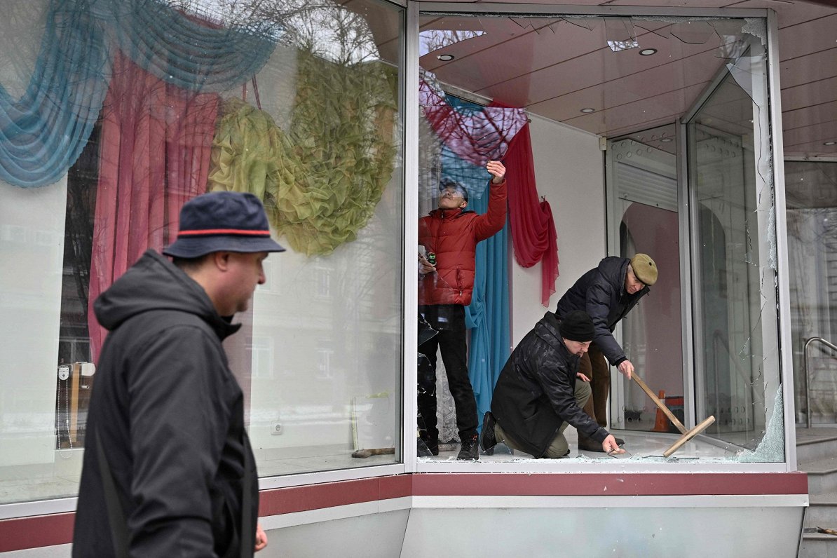 Iedzīvotāji sakopj veikala skatlogu pēc Krievijas uzbrukumiem Hersonā, 2023.gada janvāris