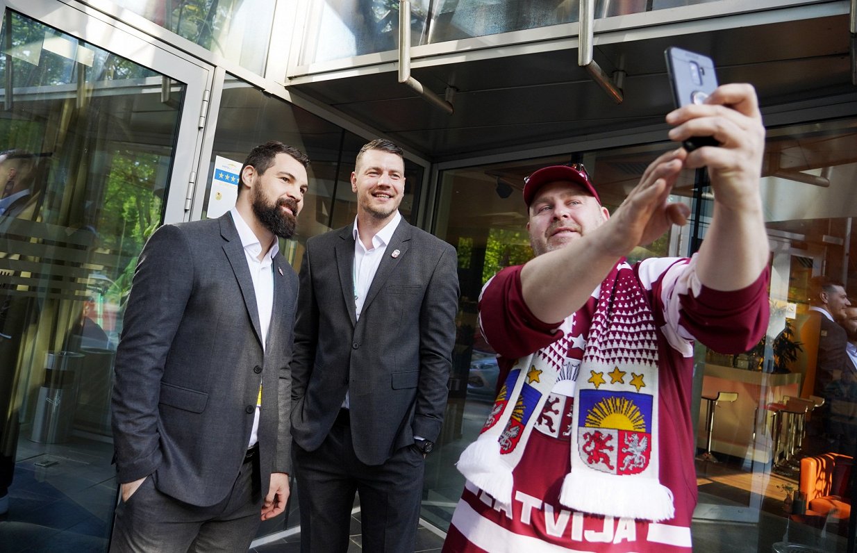 Hokejisti Kaspars Daugaviņš (no kreisās), Miks Indrašis un izlases fans pie komandas viesnīcas