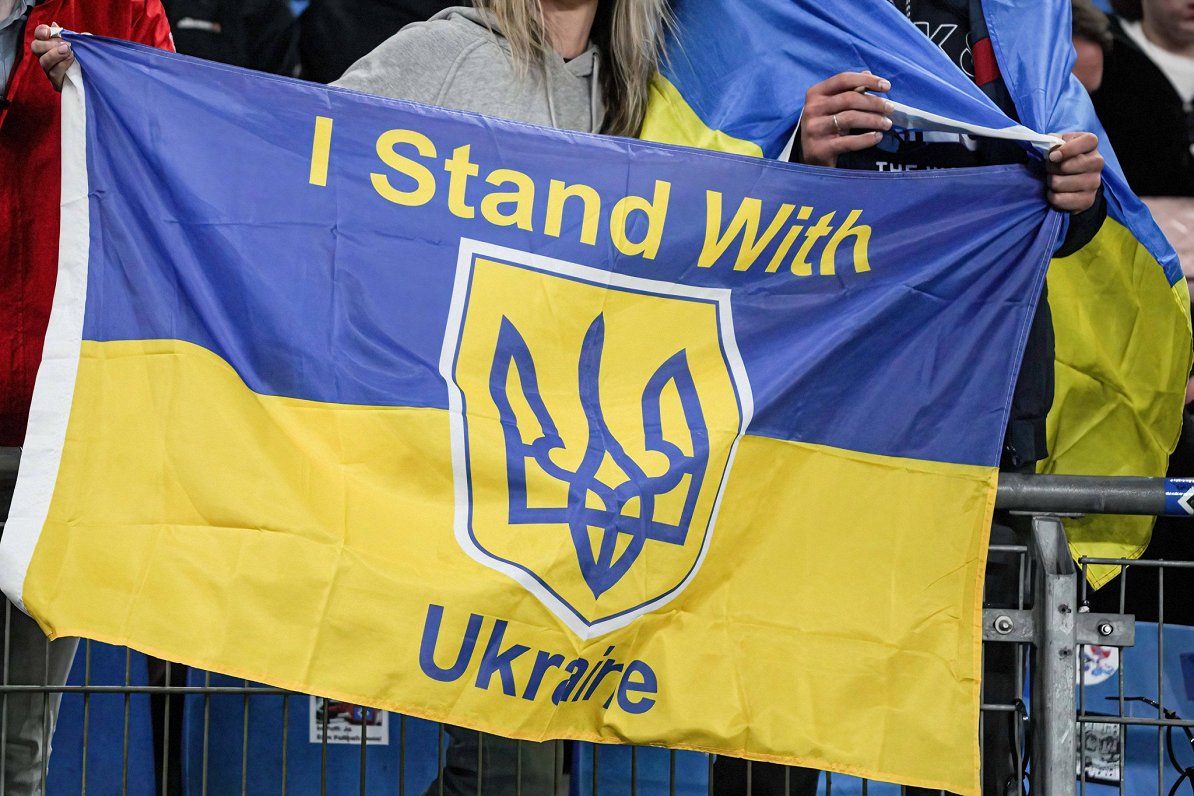 Ilustratīvs attēls: Ukrainas karogs, uz kura angļu valodā rakstīts &quot;Es atbalstu Ukrainu&quot;