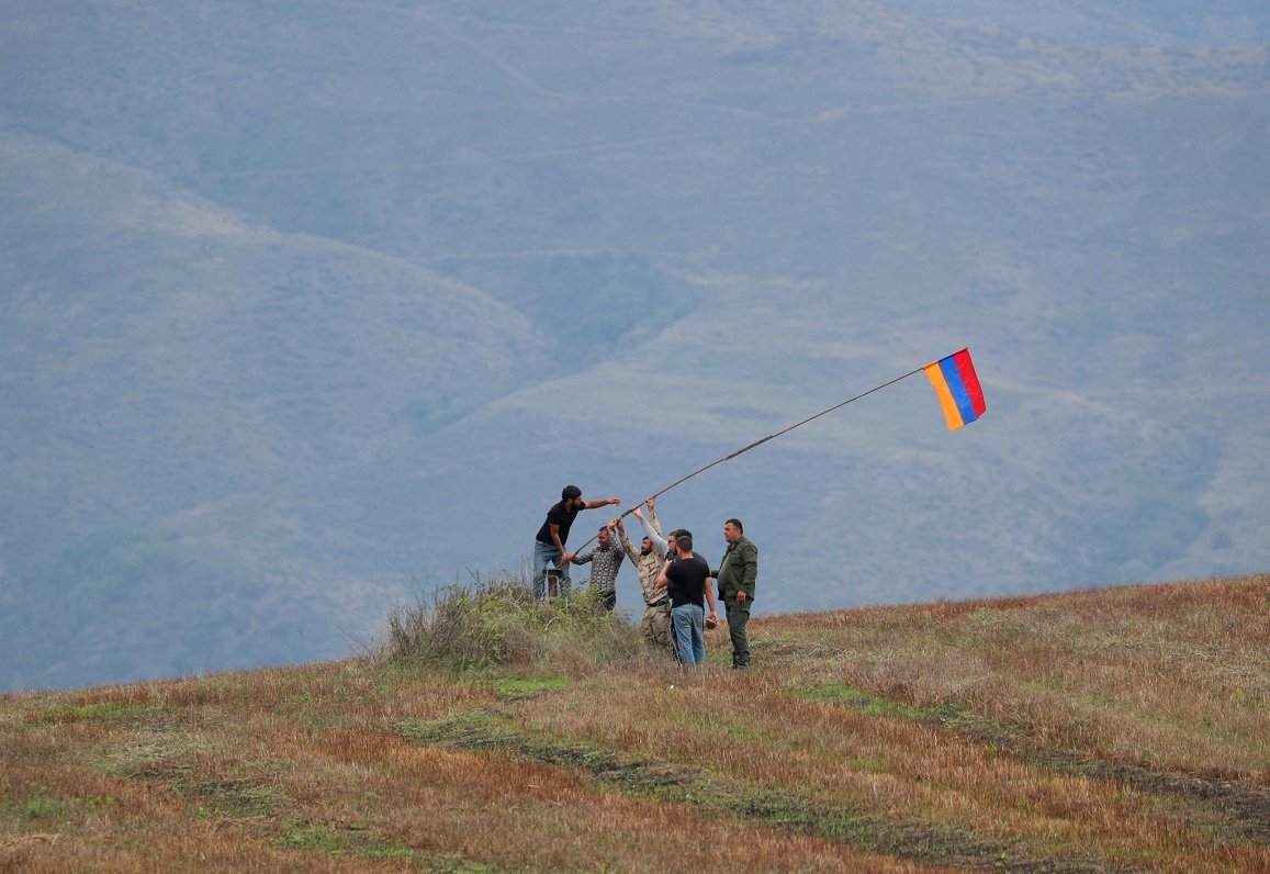Cilvēki paceļ Armēnijas karogu pie kontrolpunkta uz ceļa, kas ved uz Kalnu Karabahu