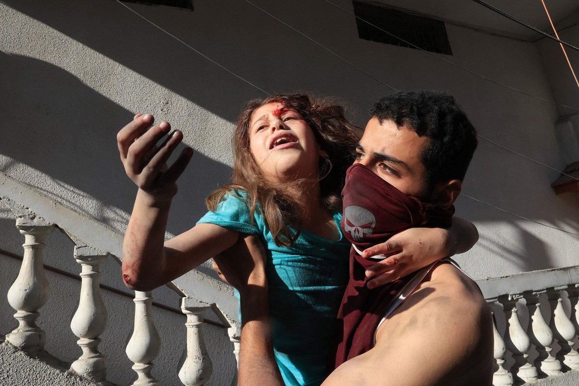 Vīrietis no ēkas drupām izceļ izglābtu palestīniešu meiteni pēc Izraēlas gaisa trieciena Rafahas bēg...