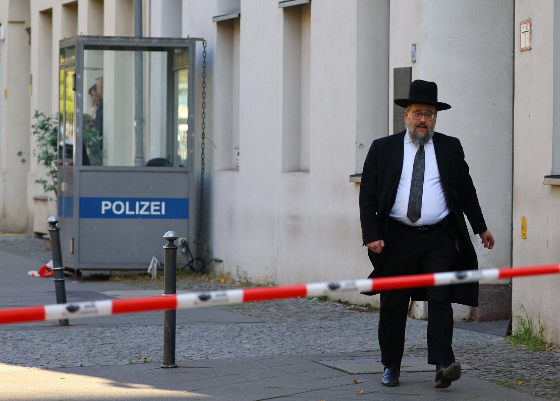 vīrietis aiz policijas norobežojuma, kas tika novilkts ap uzbrukumā cietušo sinagogu Berlīnē