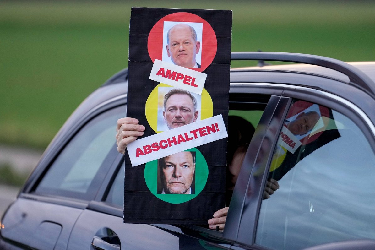 Protesta akcijas dalībnieki Vācijā demonstrē plakātu ar valdošās koalīcijas politiķiem un saukli &qu...
