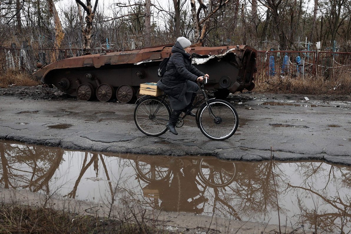Ilustratīvs attēls: Sieviete Doneckas apgabalā, Ukrainā brauc garām iznīcinātam bruņu transportam