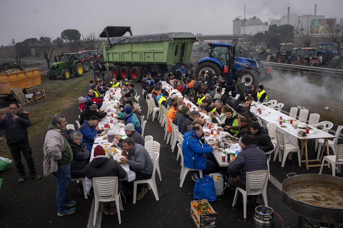 Spāņu zemnieki ietur maltīti, piedaloties protesta akcijā, kuras laikā viņi ar traktoriem bloķēja ce...