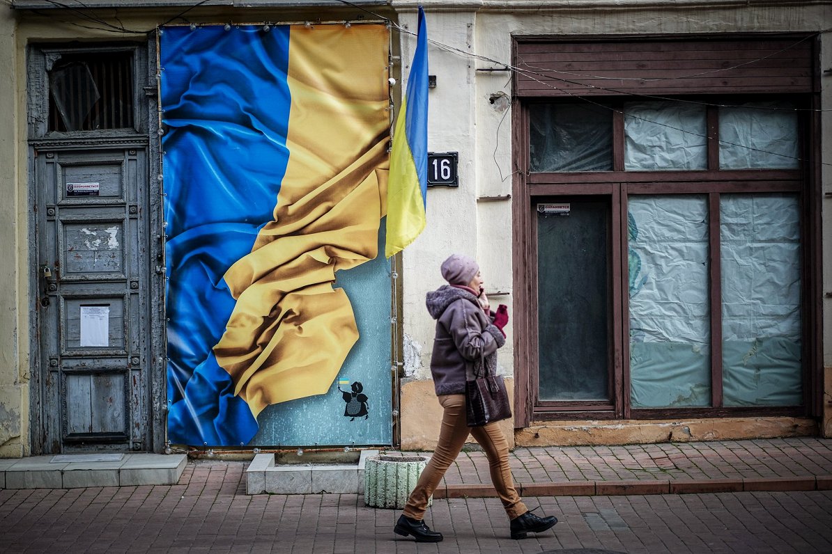 Ilustratīvs attēls: sieviete Ukrainas pilsētā Odesā blakus ukraiņu karoga attēlam uz ēkas sienas