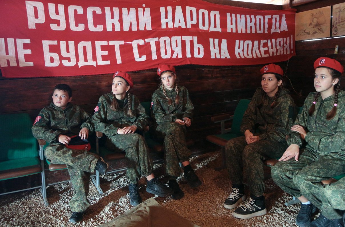 Krimas bērni, kas iesaistīti Krievijas &quot;patriotiskās audzināšanas&quot; programmā. Uzraksts pie...