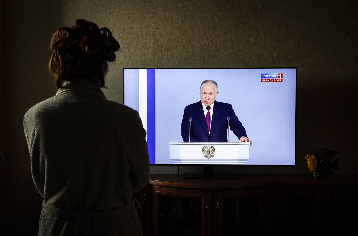 Женщина смотрит выступление диктатора Владимира Путина по телевизору