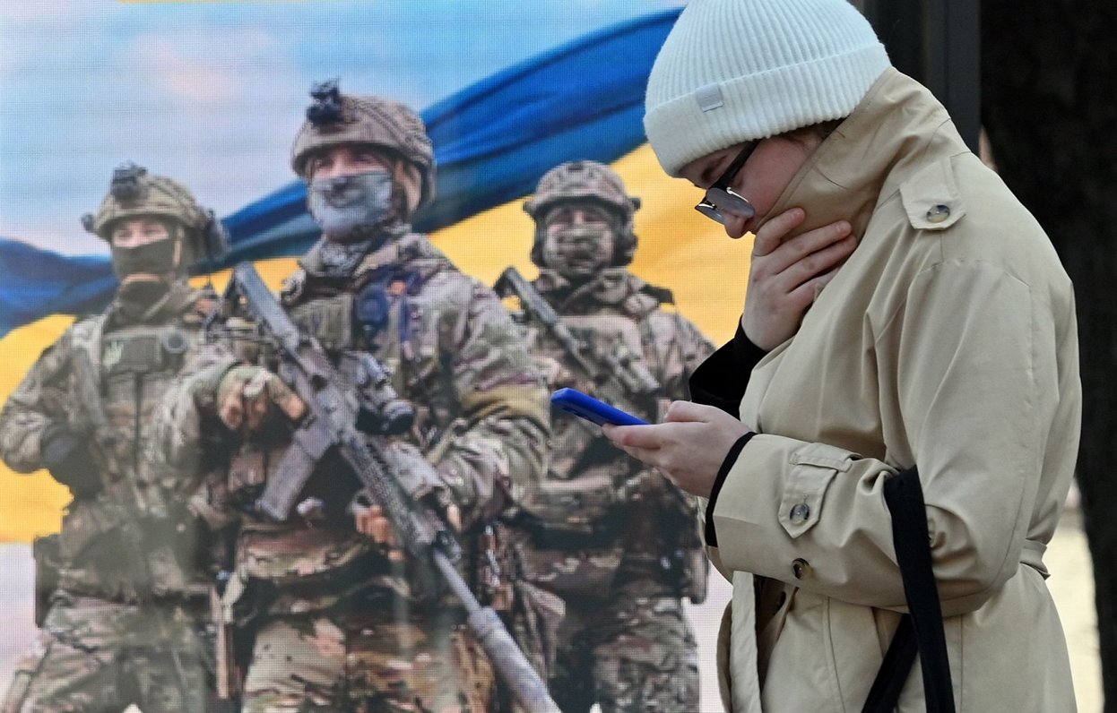 Sieviete ar telefonu pie Ukrainas armijas plakāta Kijivā.